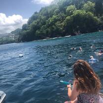 Teenage girl sits on deck of boat looking at other teens snorkeling in water