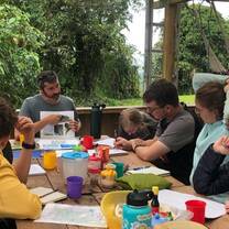 Group of teens learn lesson from teacher outside at table in rainforest