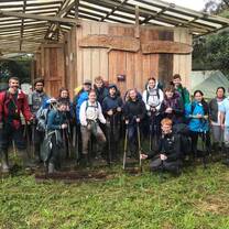 Group of teens in front of rustic lodge holding hiking poles and backpacks