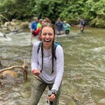 Teen girl in foreground laughs while wading across river with group in background