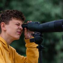 Teen boy looks through telescope in cloud forest