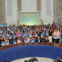 An audience of  individuals holding up certificates and smiling