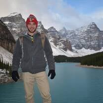 a man stands in front of a lake with snow capped mountains 