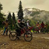 dirt bike riders pose for a photo with snow capped mountains in the background