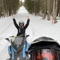two snow mobile riders take a photo on a snowy path in a forest