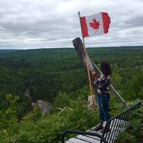 a girl stands under a Canadian flag on a hike 