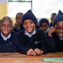 Three smiling boys in school uniforms, sitting together at a desk.