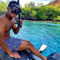 student sits in snorkle gear in front of  a body of water