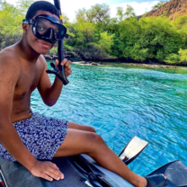 student sits in snorkle gear in front of  a body of water