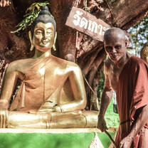 A monk sweeps the stairs beside a large golden Buddha 
