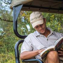 A Bushwise student pauses on a game drive to read one of his reference books.