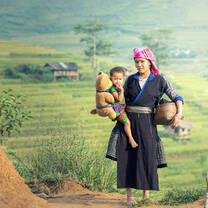 Woman holding a child in front of a background of greenery.