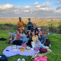 A group of students sit and stand on the lawn at a picnic