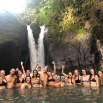 Students pose while standing in water in front of a waterfall.