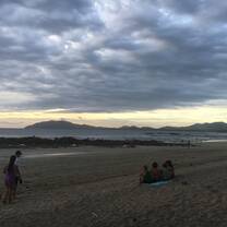 Four students sit on a towel on the beach watching the sunset over the ocean.
