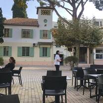 A street scene with tables and chairs on a cobblestone street, people sitting in chairs or walking