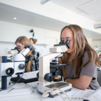 Two female students are looking through a microscope