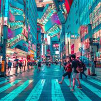 A busy street scene with a people crossing a crosswalk in the foreground, and neon-blue-hued buildings rising on all sides