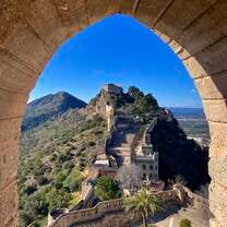 Ashley, an RVF International participant, capturing the breathtaking view of a historic castle perched on a hillside through a stone archway in Spain, showcasing the beauty and history explored while teaching abroad with RVF International.