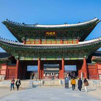 People walking into and out of a green and red Korean temple
