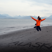 Young woman jumping on a black-sand beach in Alaska