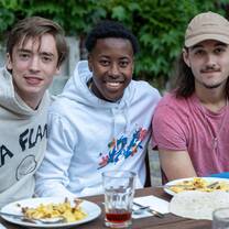 Three young male students are sitting at a table with food in front of them. They are smiling.