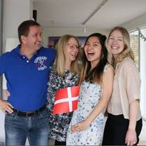 A couple, their daughter and a host student are smiling at each other. The student is holding a Danish flag. 