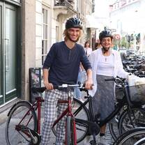 Two students are standing with bikes and smiling. They are wearing helmets. The street behind them is filled with parked bikes.