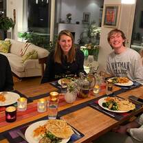 Four students are sitting around a dinner table. There are plates of food in front of them and candles on the table. It looks warm in cosy.