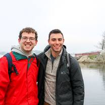 Two young men are standing in front of a lake. 