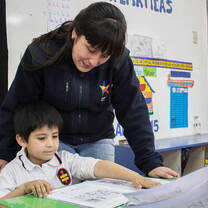 A volunteer teacher working with a child in a classroom.