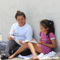 Volunteer teacher with a child who is reading, sitting outside in the sun.