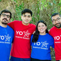 Four volunteers of América Solidaria hugging, wearing t-shirts with the organization's logo.