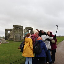 A group of students taking a selfie using a selfie stick in front of Stonehenge 