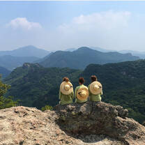 Three students sitting at the top of a mountain overlooking mountains in the distance