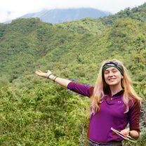 A woman pointing to a green valley behind her