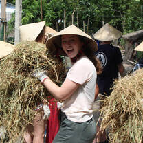 A student wearing a Nón lá, carrying a stack of wheat