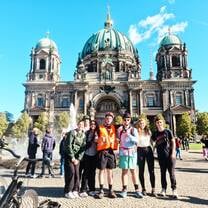 A group wearing bike helmets poses for a photo in front of Berlin Cathedral 