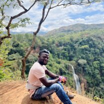 man sitting on a cliff in front of a forest