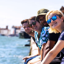A group of smiling students in a row on a wall of the Venice Canal.
