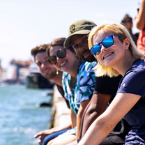 Summer students smiling on Venice canal wall.