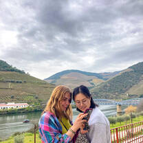 Two students looking at something on a smartphone, mountains behind them in the distance