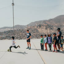 A child kicking a ball and a group of kids in line waiting for their turn