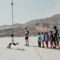 A child kicking a ball and a group of kids in line waiting for their turn
