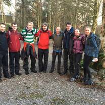 Group of young people in hiking gear. Standing in a line with arms around each other, looking happy.