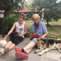 Two volunteers sit with two dogs 