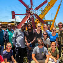 A group of people posting in front of a rusty windmill.