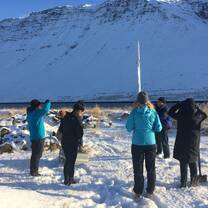 A group of students wearing cold-weather clothing standing before a snow-capped hill.