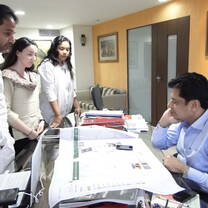 Three students standing before a man sitting at a desk, papers spread before him