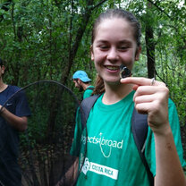Teen wearing Projects Abroad Tshirt, holding butterfly in forest